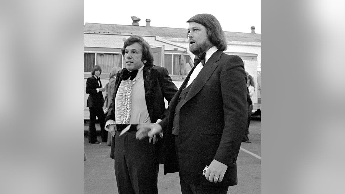 布萊恩·威爾遜(Brian Wilson)穿著燕尾服的布萊恩·威爾遜(Eugene Landy)站在褲子附近,調整了褲子。