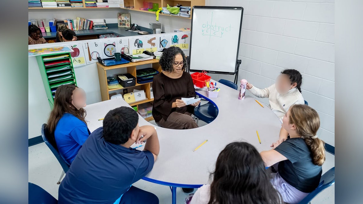 teacher at round table with five kids in a classroom