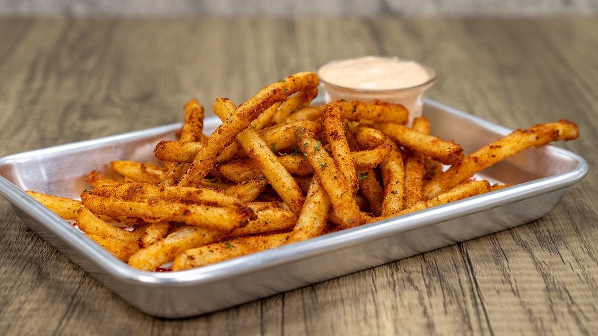 Crispy French fries on a tray with dipping sauce seen on table.
