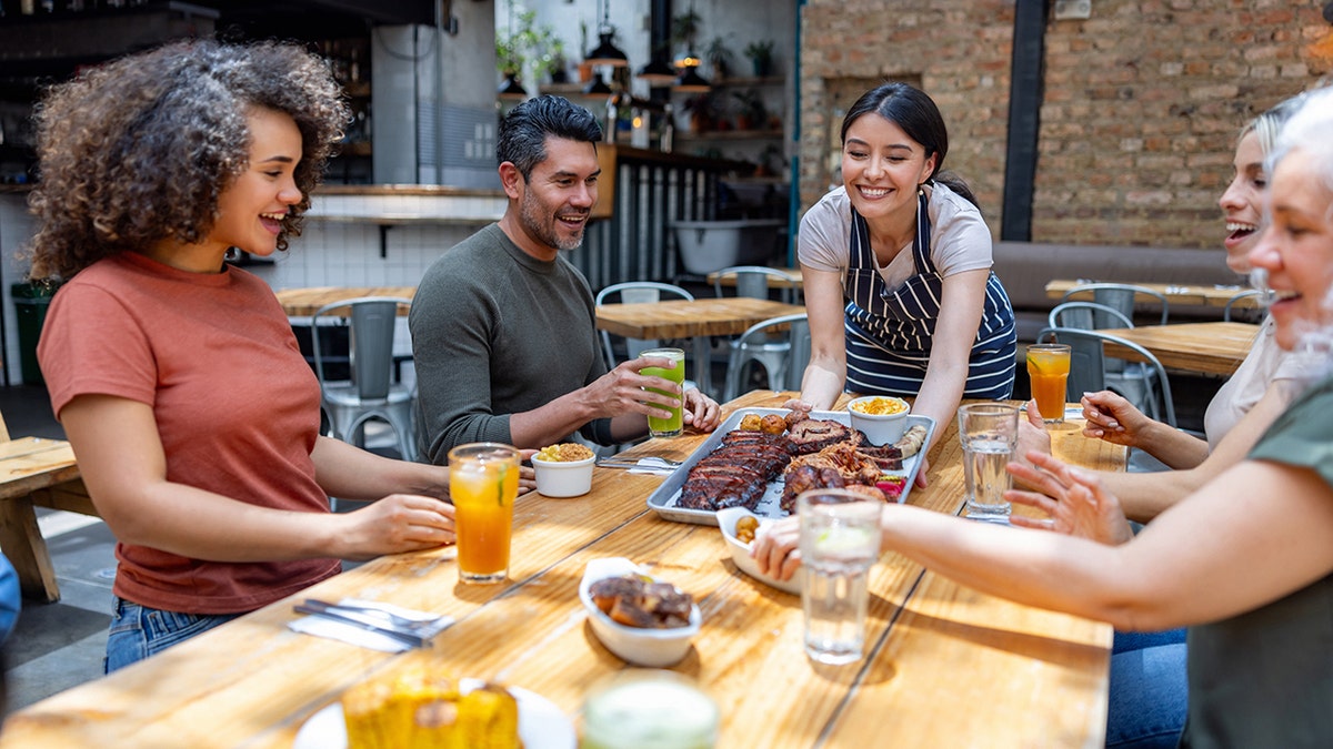 Friends smiling being served meat at restaurant by waitress