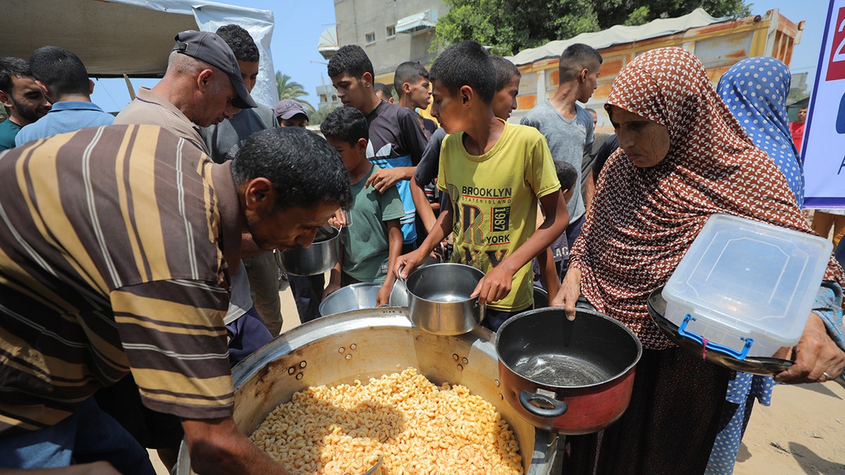 DEIR AL BALAH, GAZA - AUGUST 10: Palestinians wait with pots in their hands as a charitable organization distributes food.