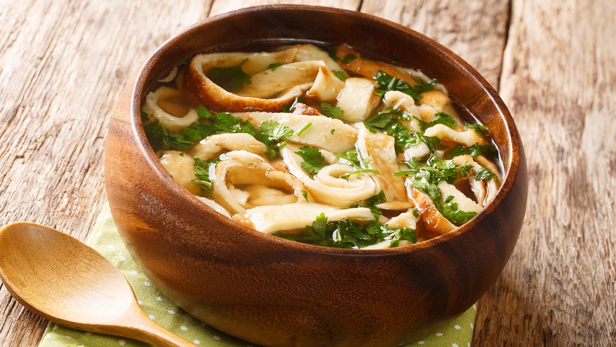 Bowl of traditional German/Austrian pancake soup seen in wooden bowl. Thin strips of pancakes seen in beef broth with fresh herbs