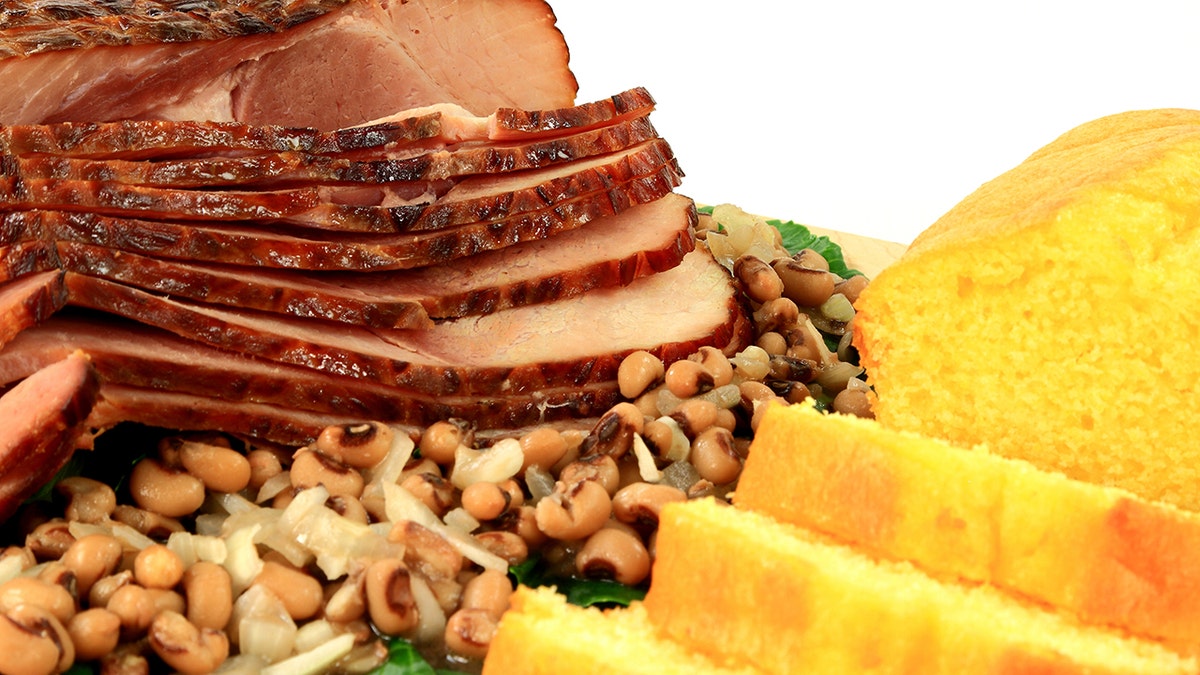 Country ham, black eyed peas and cornbread against a white background.