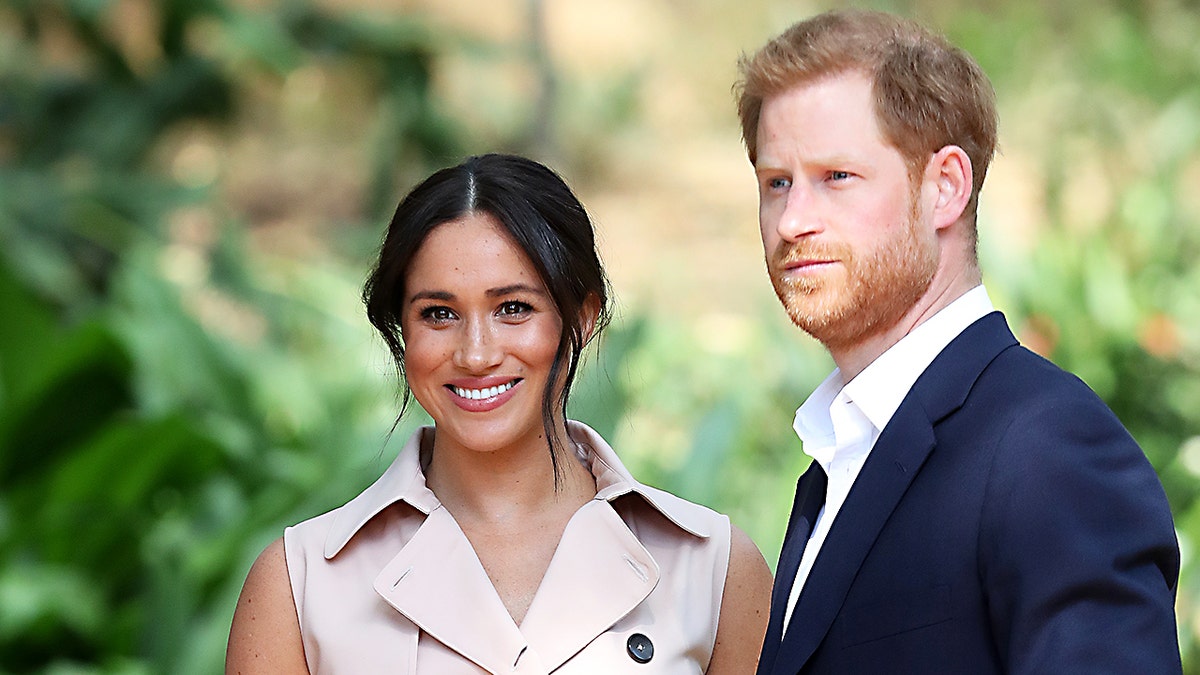 Meghan Markle smiling next to Prince Harry in a suit looking pensive.