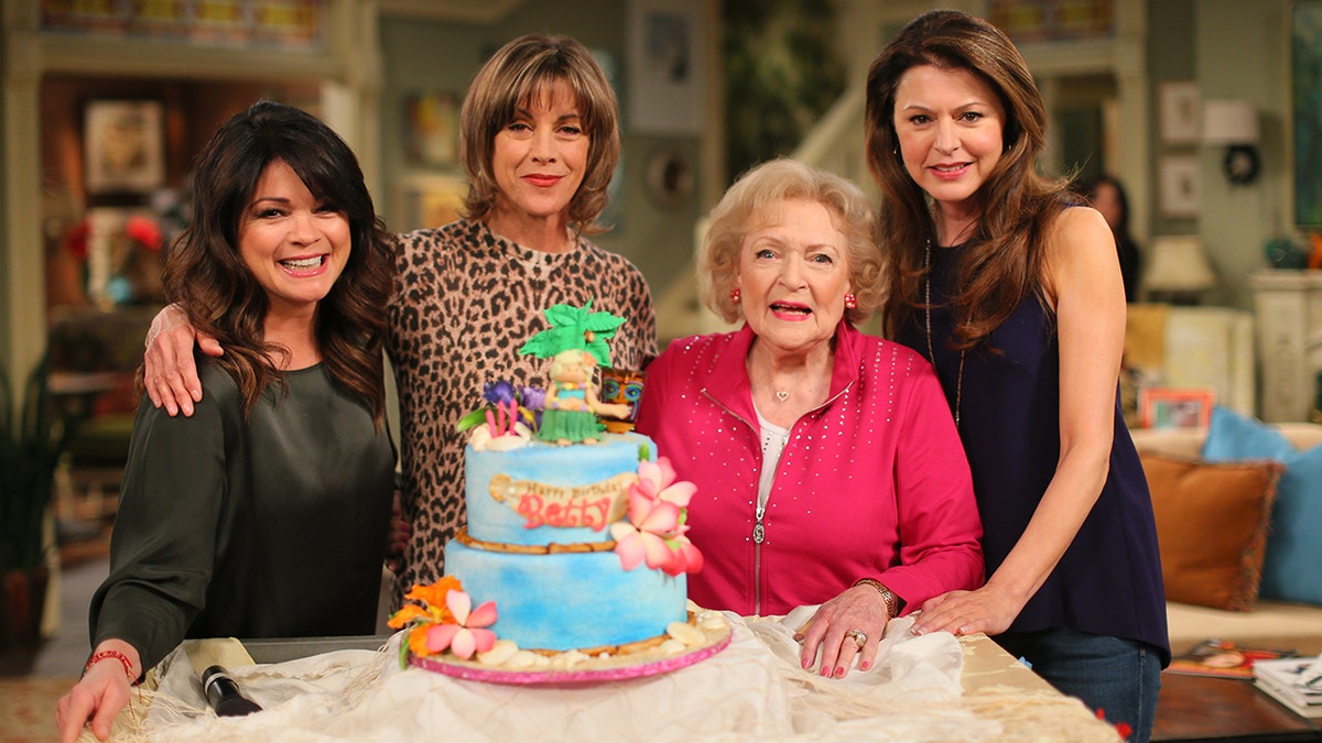 The cast of "Hot In Cleveland" posing in front of a birthday cake while on set.