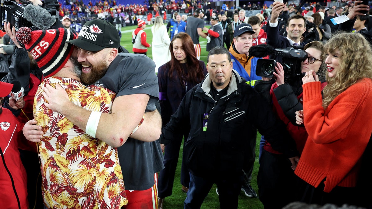 Jason Kelce and Travis Kelce hug while Taylor Swift stands nearby