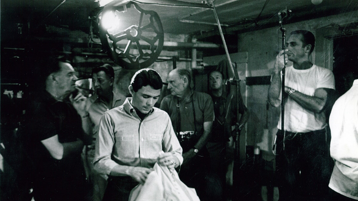 Jay Sebring at a film studio looking down holding a towel and wearing a white shirt.