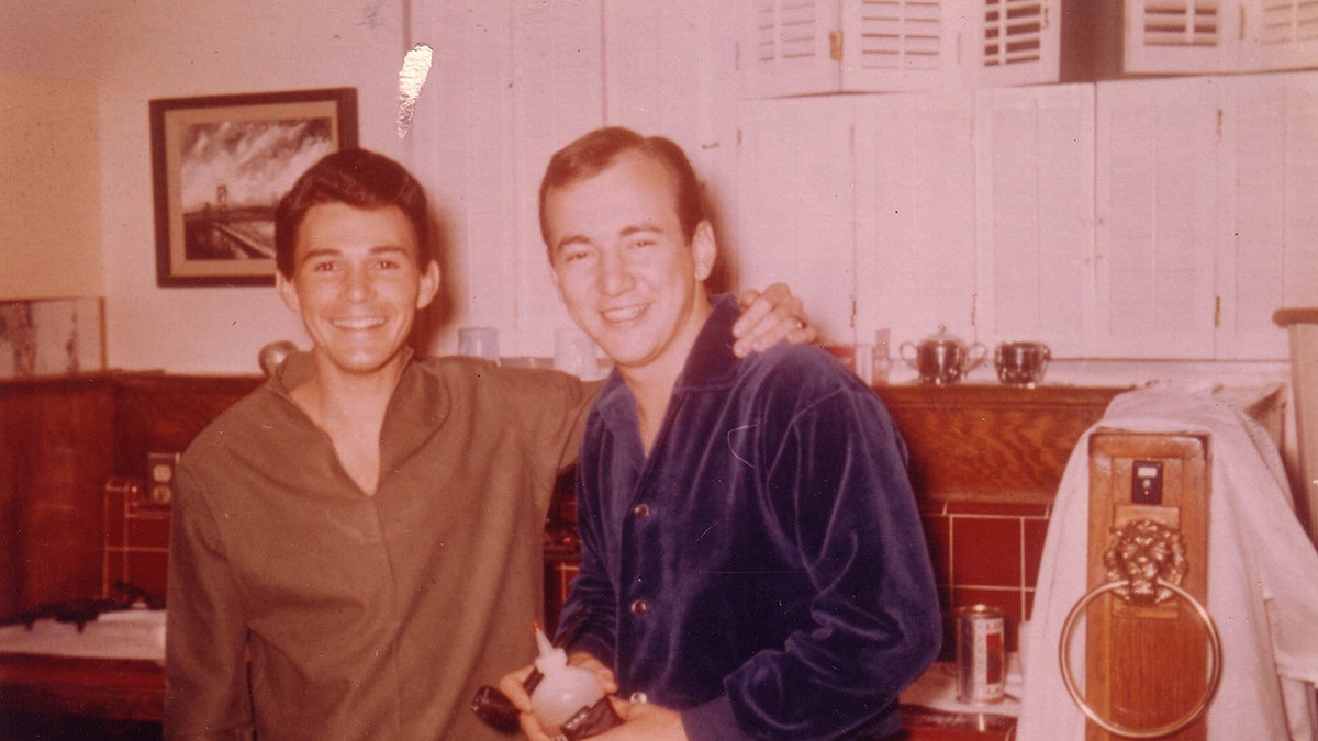 Jay Sebring with an olive-colored shirt smiling next to Bobby Darin wearing a blue velvet suit.