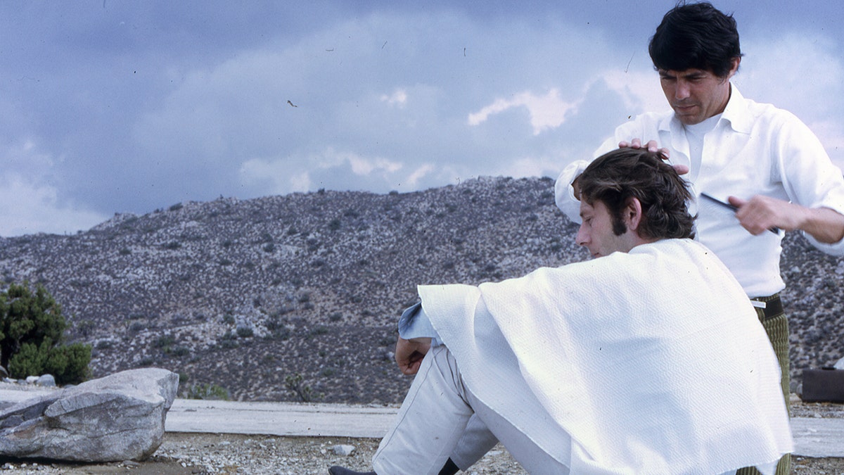 Jay Sebring giving Roman Polanski a haircut outdoors.