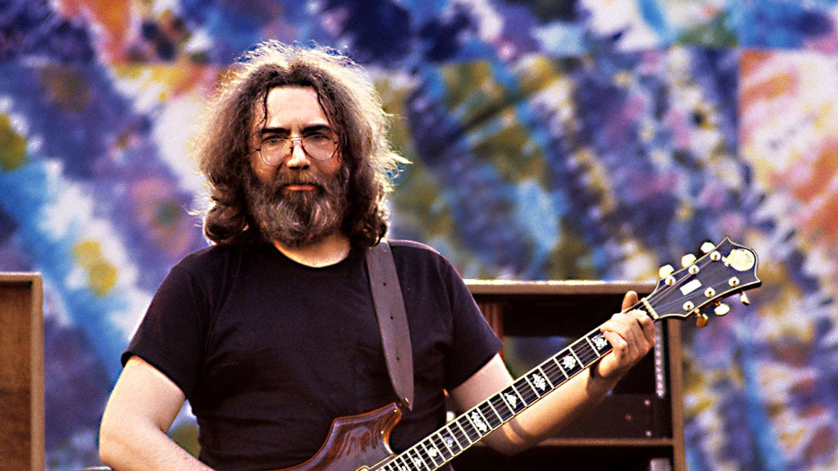 Jerry Garcia of Grateful Dead playing guitar in front of tie dye.