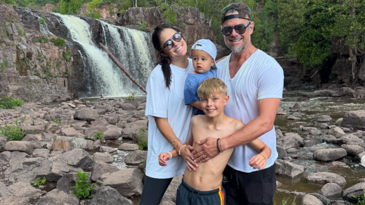 Josh Duhame poses in front of a waterfall with his wife and kids.