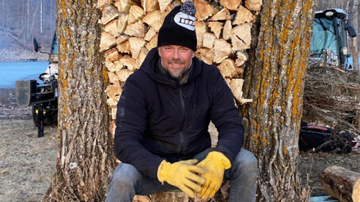 Josh Duhamel smiles as he poses in front of a stack of logs at his Minnesota home. 