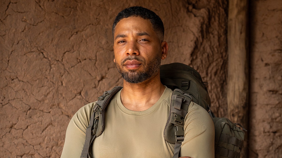 Jussie Smollett crosses his arms wearing a green shirt and backpack
