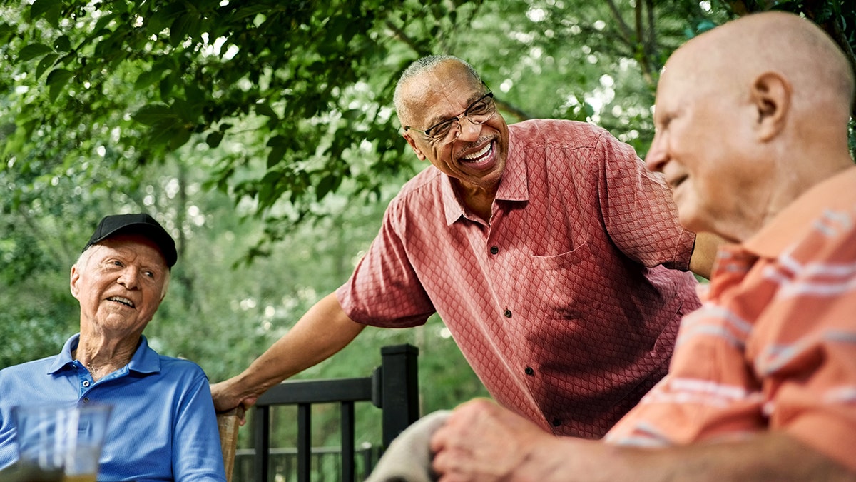 Group of happy senior men gathered around a table in a backyard.