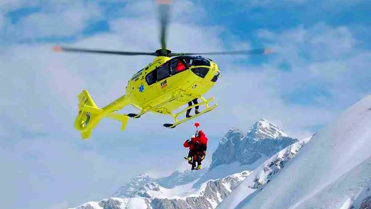 A yellow helicopter picking up two people in mountains