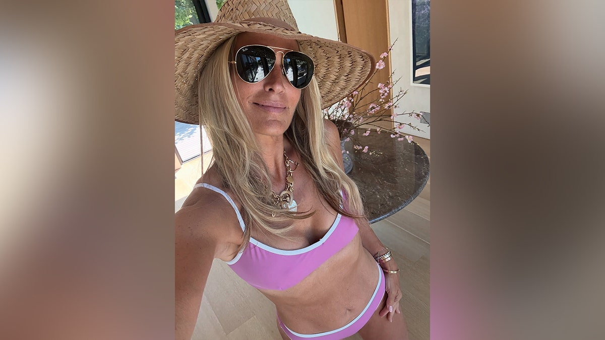 Molly Sims wearing a purple bikini with a sunhat and black sunglasses.