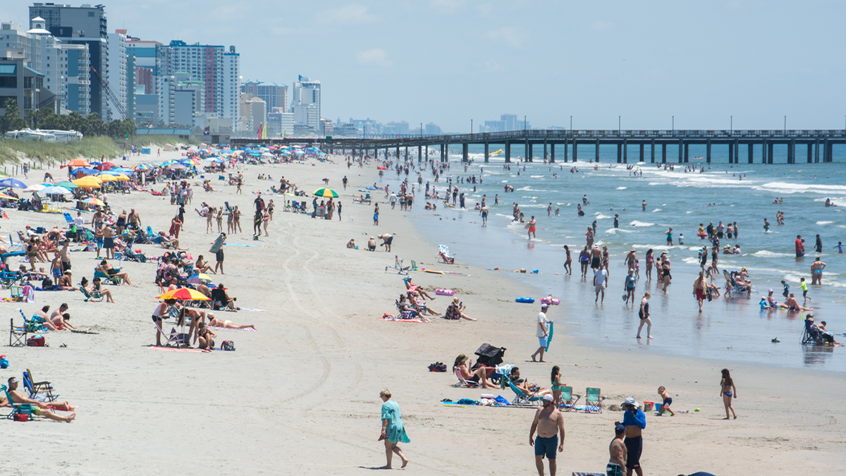 a wide shot showing dozens of beachgoers in the sand near the Myrtle Beach pier in South Carolina