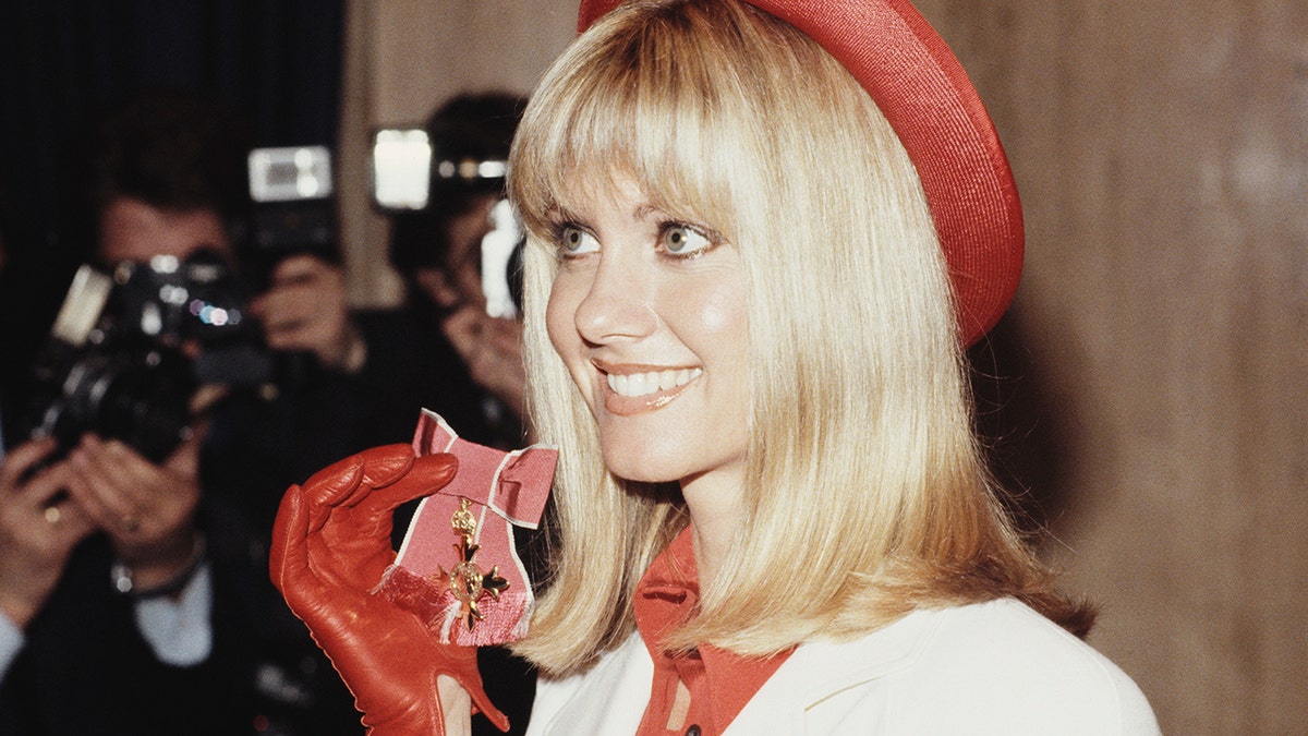 Olivia Newton-John smiling and holding a medal.