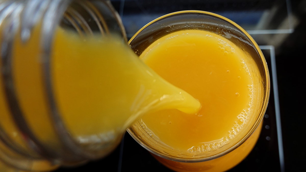Orange juice being poured into a glass, seen up close from above