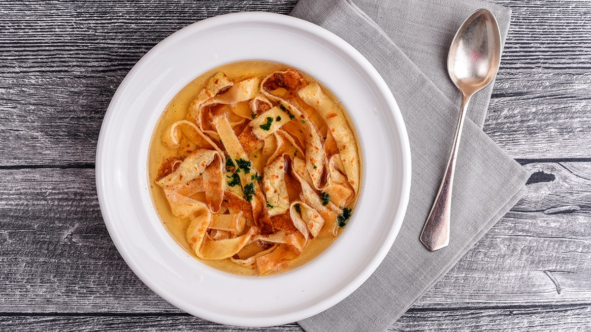 Pancake soup, also known as "flaedlesuppe," is shown in a bowl next to a silver spoon.