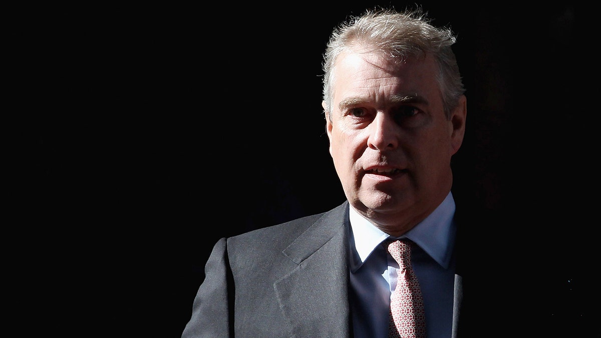 Prince Andrew wearing a dark suit looking serious behind a black background.