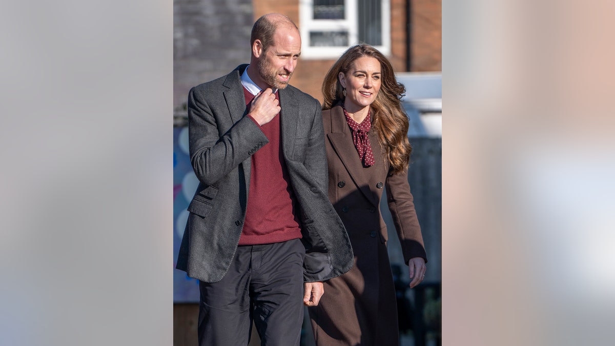 Prince William wearing a grey blazer and a burgundy sweater walking alongside Kate Middleton in matching attire.