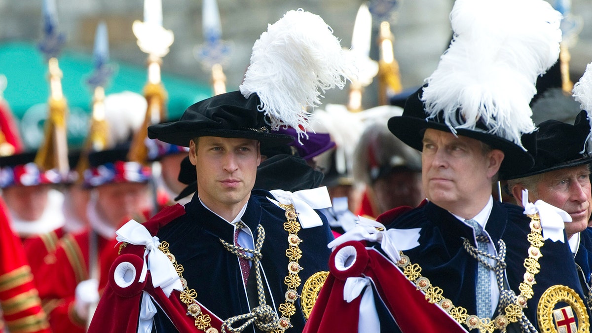 Prince William and Prince Andrew looking serious in royal robes marching outdoors.