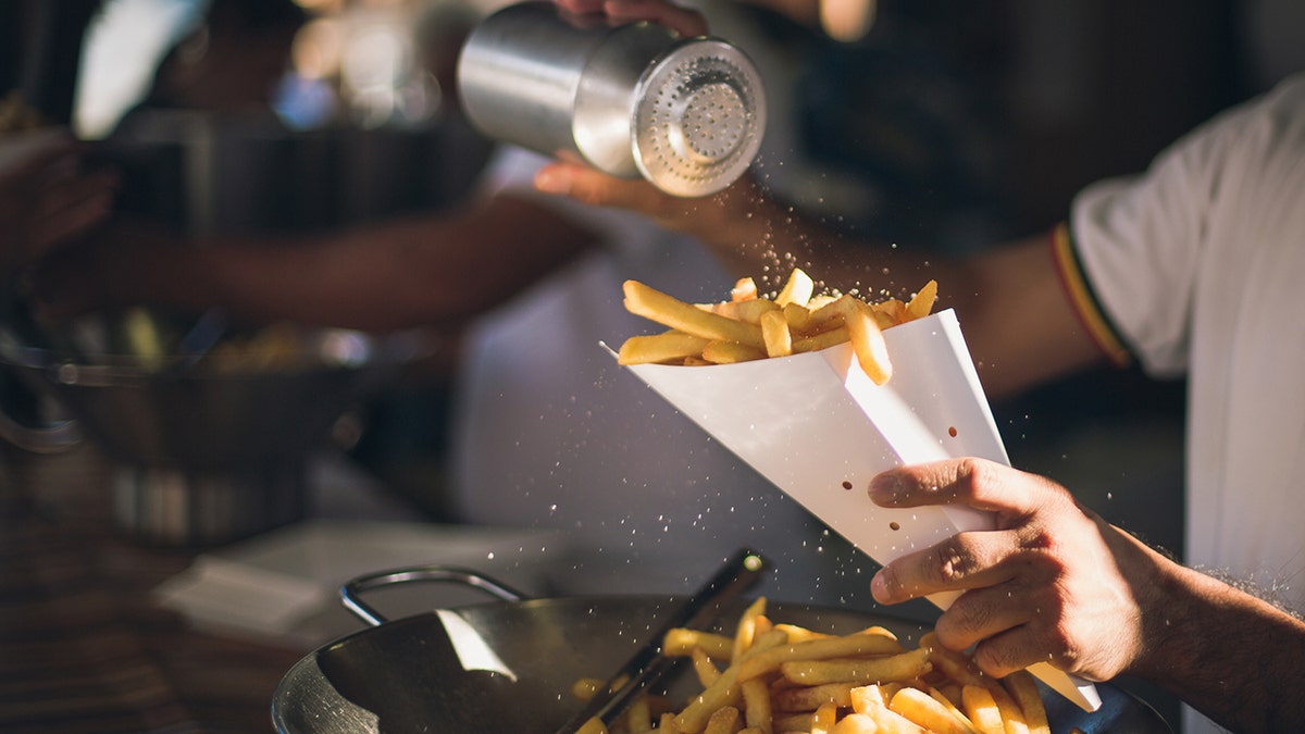 Worker sharking salt in french fries that are being served in paper cone in Italy