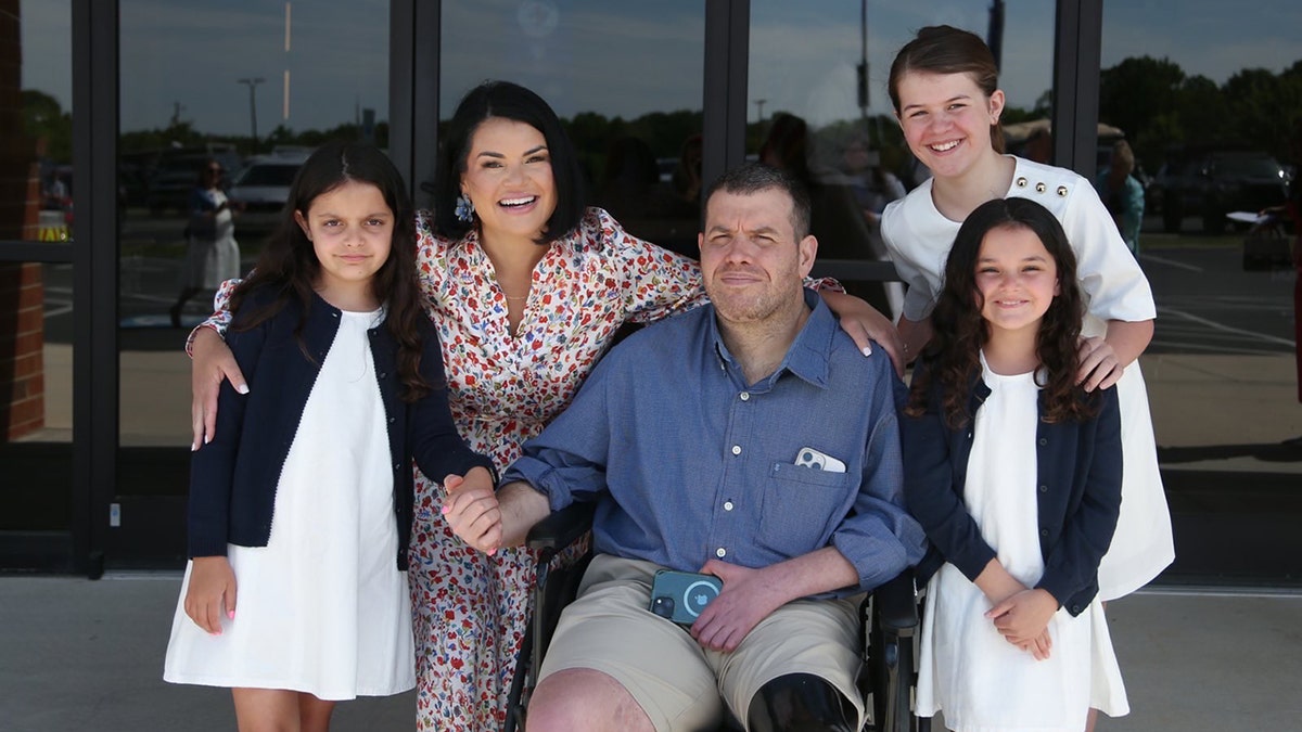 Michael Ferardo with the wife Sarah and their three daughters outside a building smiling together.