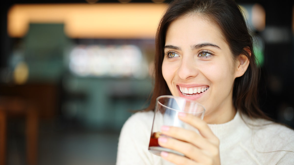 A smiling woman holds a glass of soda in her hand.