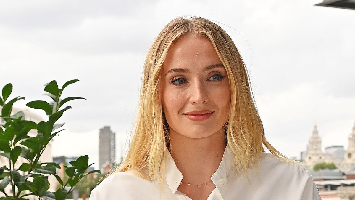 Sophie Turner wears a white blouse with a necklace