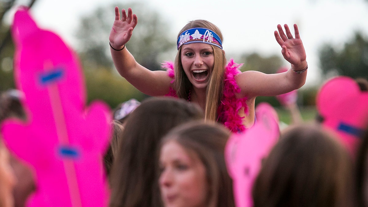 Girl seen above crowd during Sorority Bid Day at George Washington University, wearing Alpha Phi headband with pink signs and accessories around her