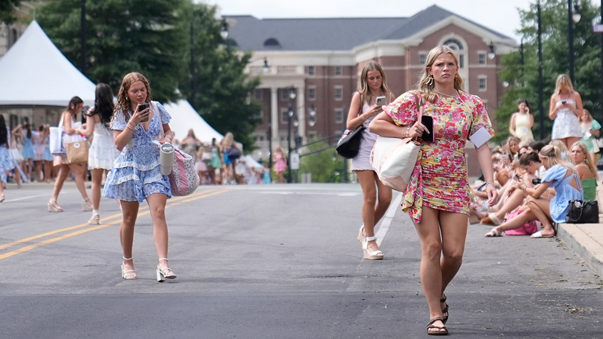 Sorority recruits walk near sorority row at the University of Alabama, Thursday, Aug. 14, 2025 in Tuscaloosa, Ala., seen on phones and in floral dresses