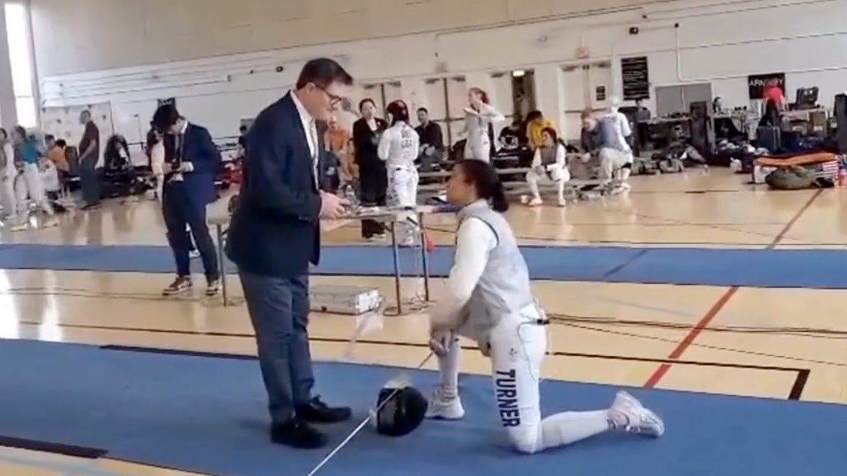 Fencer Stephanie Turner kneeling in front of a USA Fencing official
