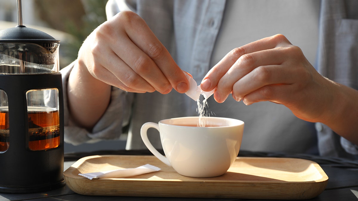 person adding sugar into cup of tea