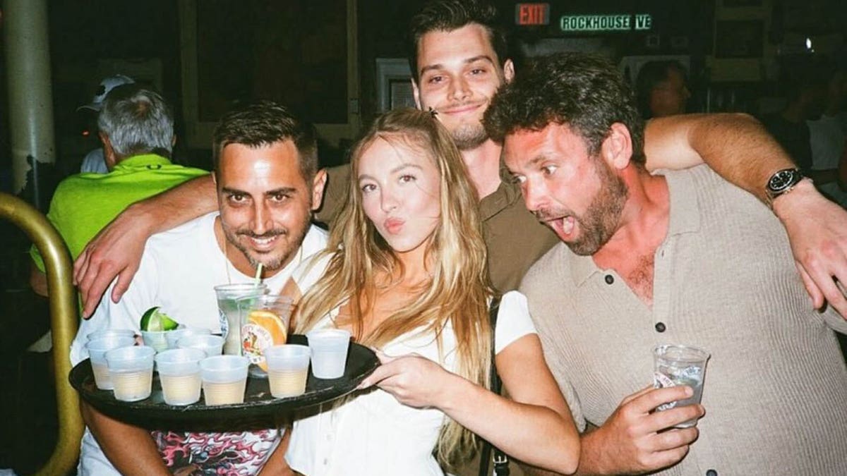 Sydney Sweeney holding a tray of drinks and posing with friends.
