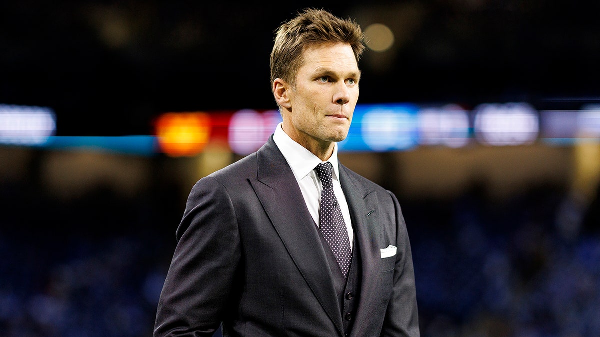 Tom Brady looks on field in suit