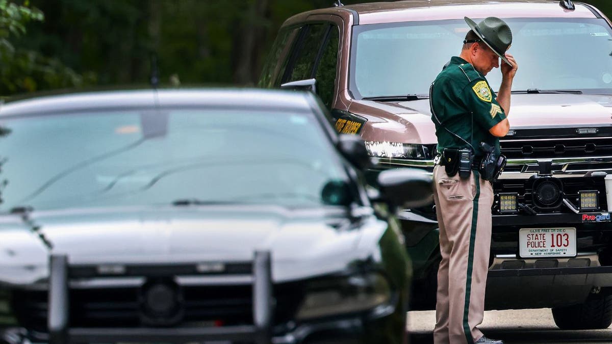 New Hampshire state trooper adjusts his hat outside police vehicles after an apparent murder-suicide in Madbury on Aug. 19, 2025.