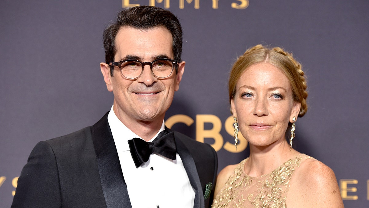 Mūsdienu ģimenes zvaigzne Ty Burrell nēsā melnu smokingu uz Emmys sarkanā paklāja ar sievu Holiju.