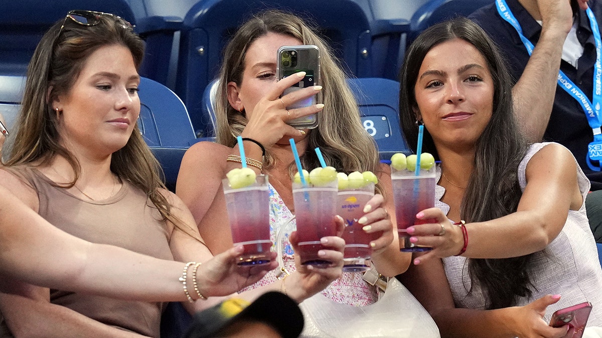 Women drinking Honey Deuce cocktails at US Open, seen sitting in stands as one takes photo of the drinks