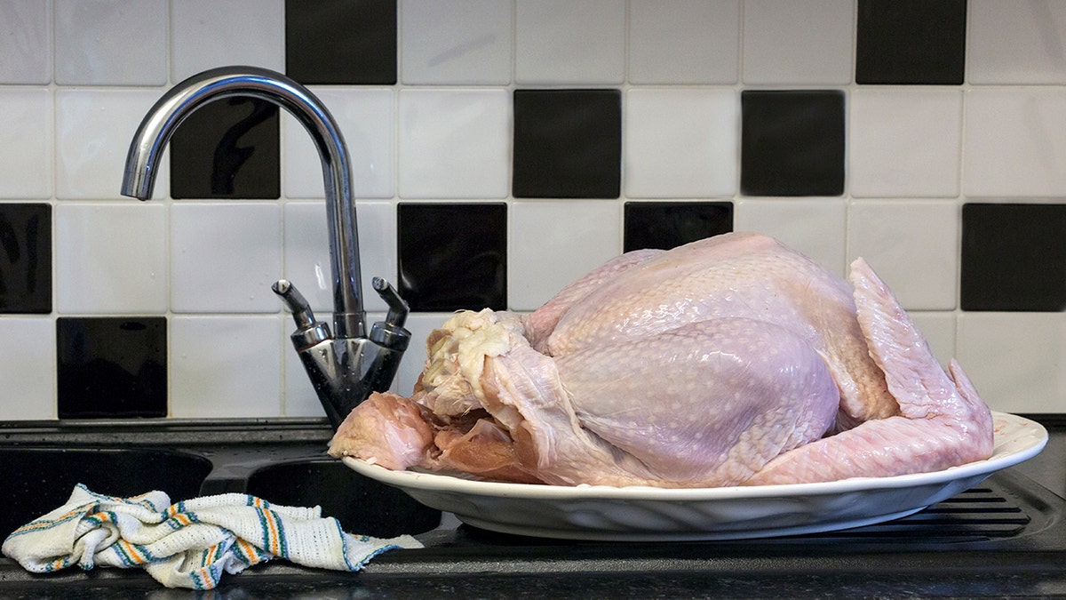 Overall, the raw chicken is on a plate next to the kitchen sink.
