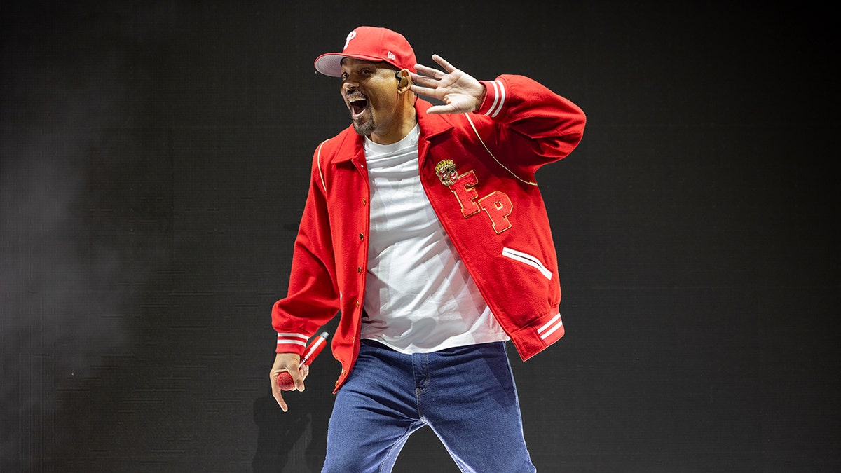 Will Smith sports red jacket and hat on stage during concert.
