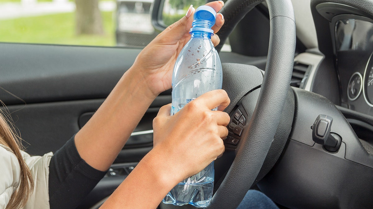 Woman's hands seen up close opening water bottle in driver seat of car.