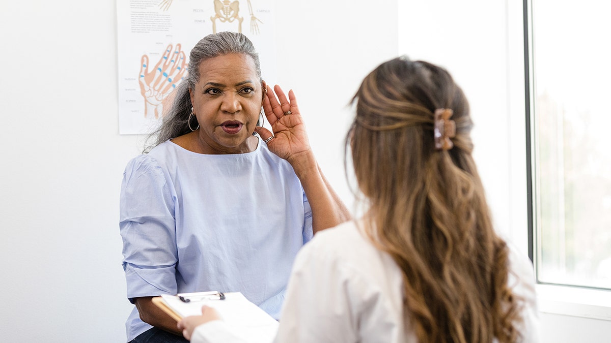 woman places hand on ear to better hear doctor