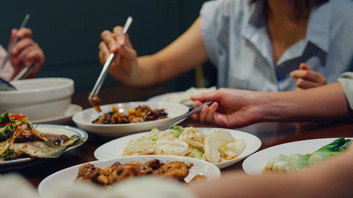 Closeup of Asian family eating chinese food and having fun dinner sitting at dining table at backyard outside home at night.