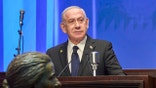 Israeli Prime Minister Benjamin Netanyahu stands at a podium speaking into a microphone
