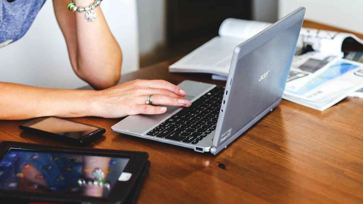 A woman types on a laptop on a wooden table.