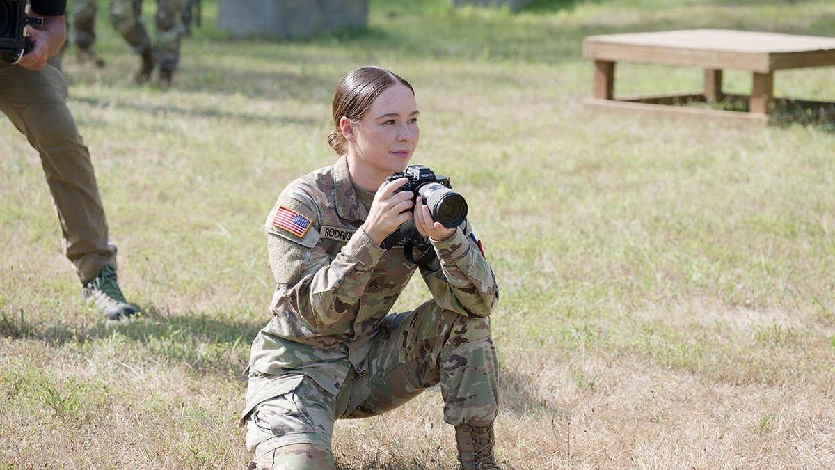 Alexia Rodrigues holding a camera in military gear.
