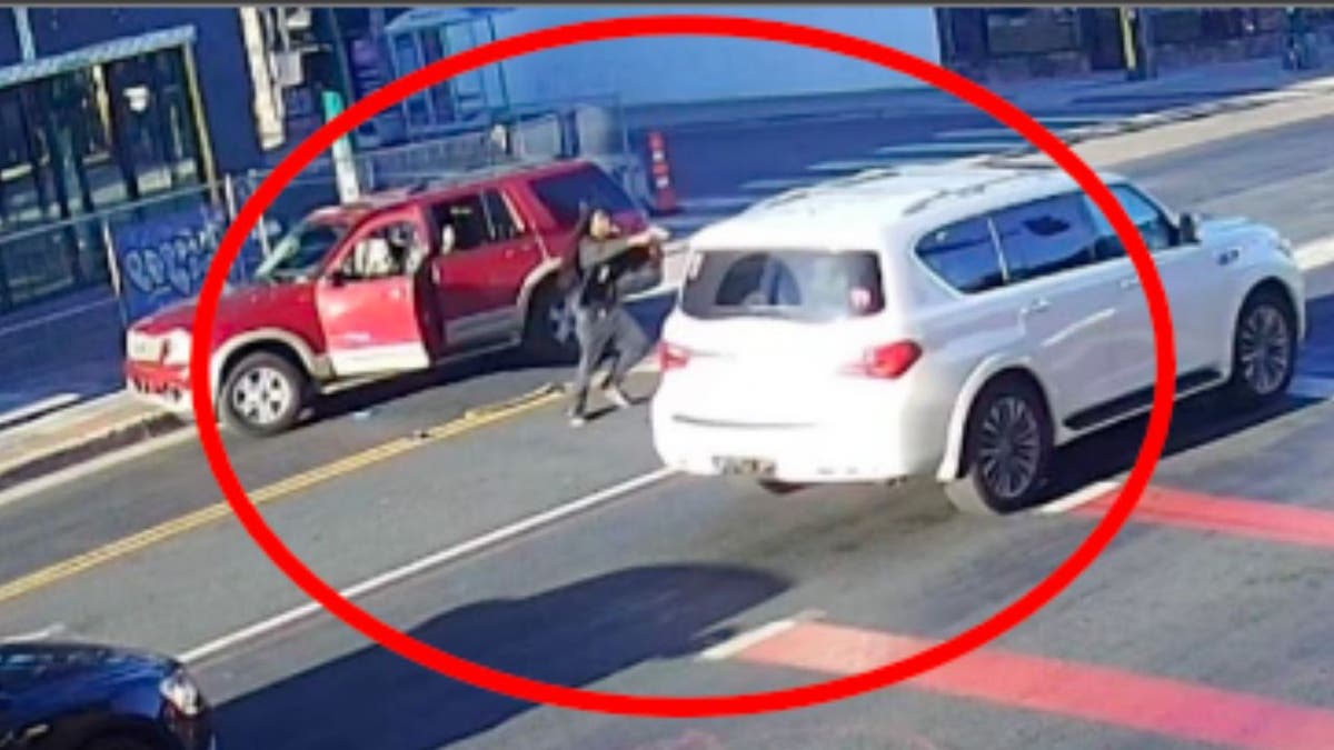 Surveillance still of alleged carjacker pointing gun at white SUV with red SUV door open.