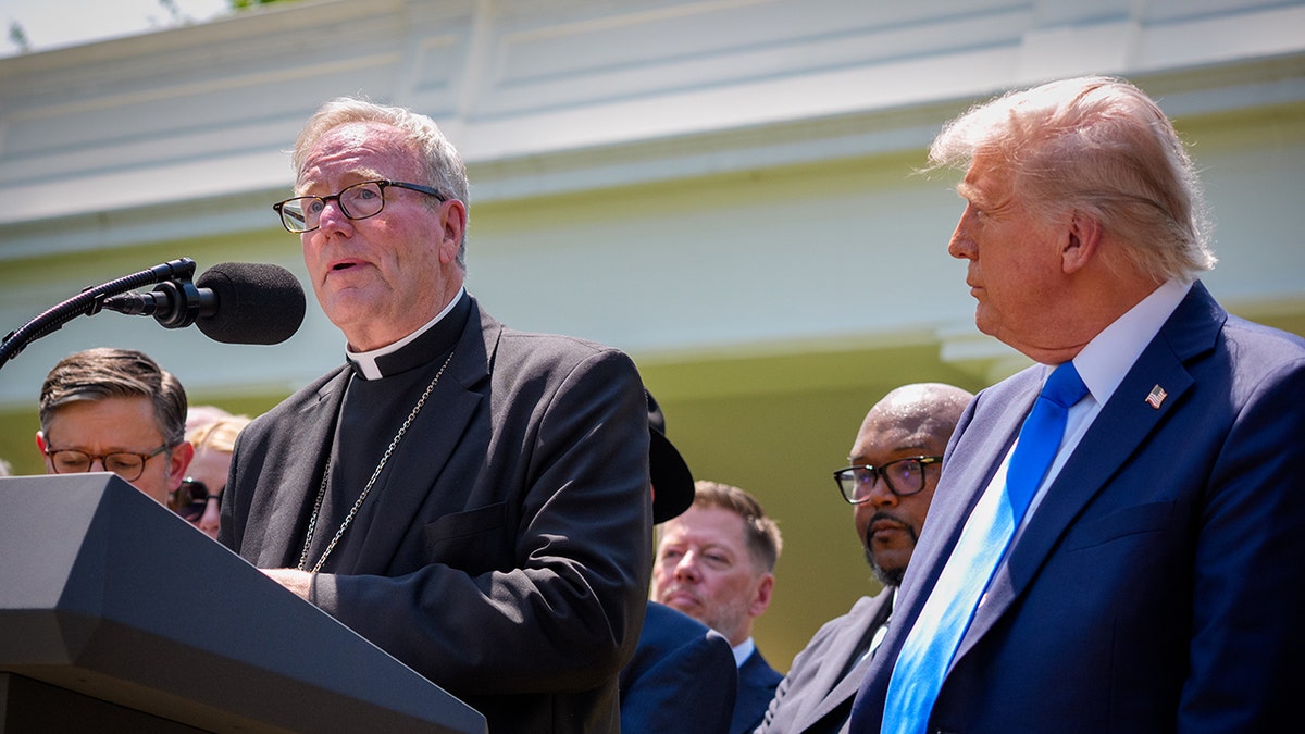 Bishop Robert Baron speaks on the White House platform while President Donald Trump listens to the prayer gathering.
